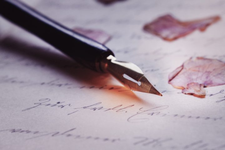 A calligraphy pen lays on a piece of paper with writing on it.