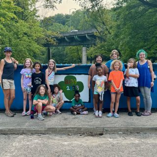 Girl Scouts and their moms pose for a group photo in front of the Young Masters Wall, located on the blue Richard McAteer Memorial Bridge on the Karl Stirner Arts Trail in Easton, Pennsylvania.