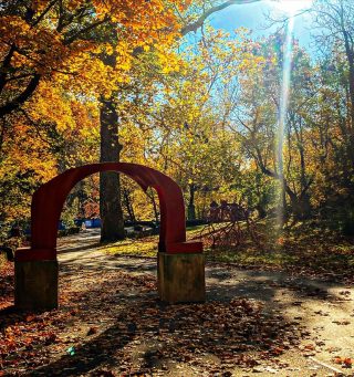 The iconic red arch sculpture and Steve Tobin's Late Bronze Root Sculpture stand near each other in autumn on the Karl Stirner Arts Trail in Easton, Pennsylvania.