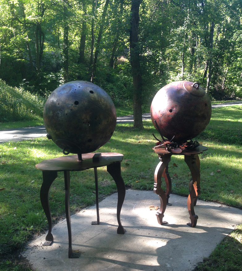 The sculpture Hydrogen and Nitrogen by David Kimball Anderson on the Karl Stirner Arts Trail Artist in Easton, Pennsylvania, featuring two balls made of patinated steel, each on its own pedestal.