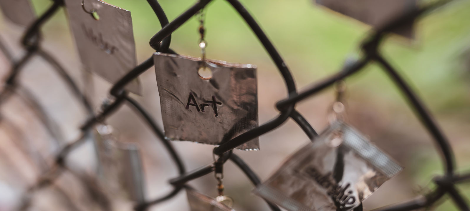 A closeup of a chainlink fence with thin metallic square hanging on it that says Art on the Karl Stirner Arts Trail in Easton, Pennsylvania