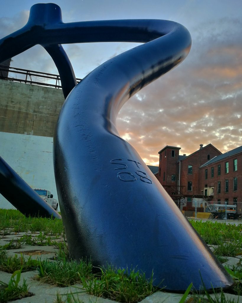A winding metallic sculpture by Stephen Tobin with a brick building in the background on the Karl Stirner Arts Trail in Easton, Pennsylvania