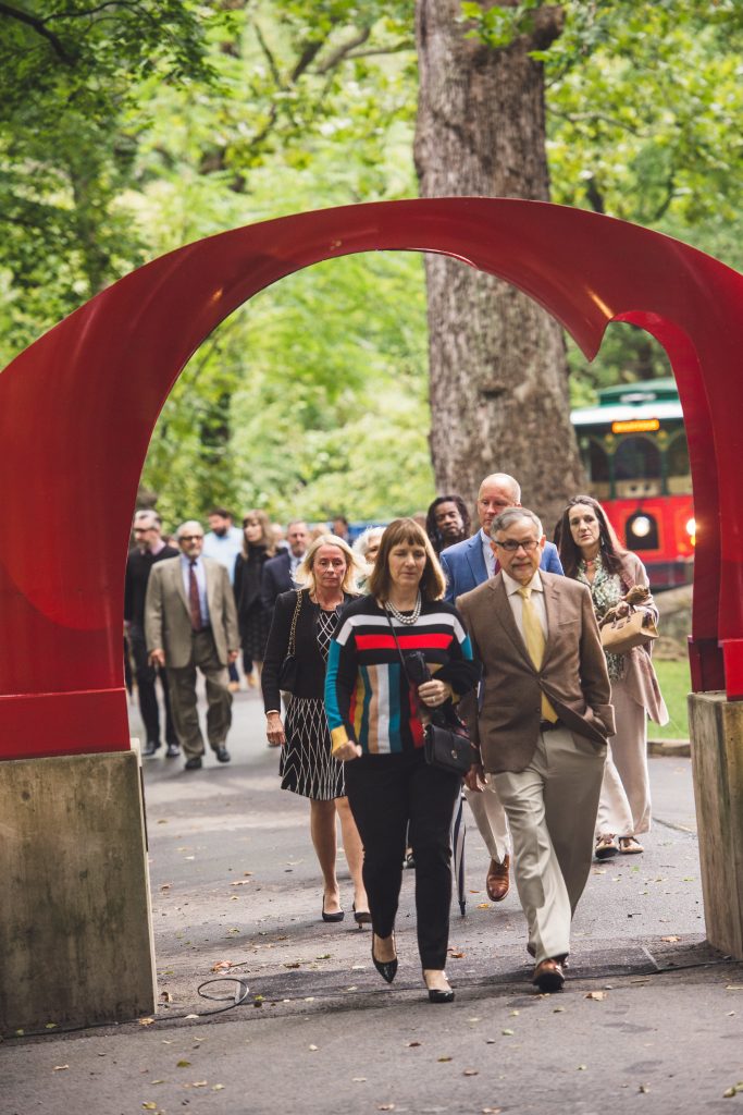 Lafayette College President Alison Byerly leads a group of people walking toward the red arch sculpture and toward the evening gala supporting the Karl Stirner Arts Trail in Easton, Pennsylvania.