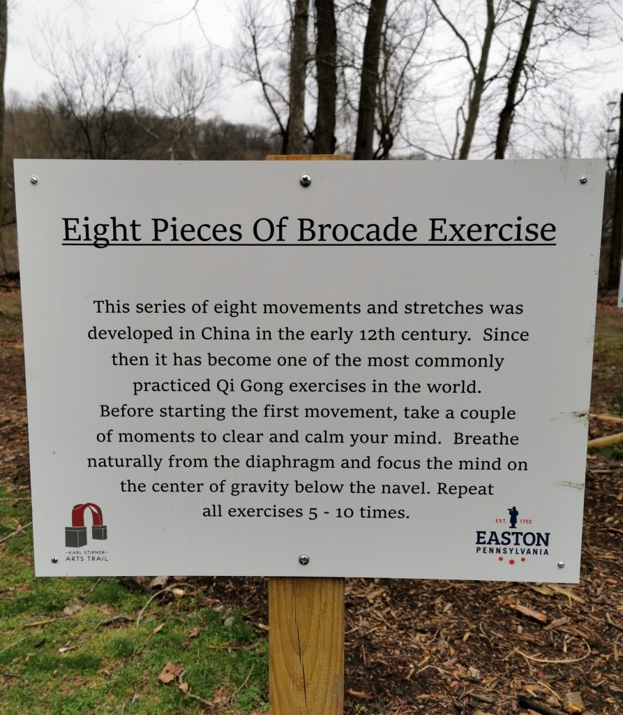 A sign with the words Eight Pieces of Brocade Exercise along with words of explanation on the Karl Stirner Arts Trail in Easton, Pennsylvania