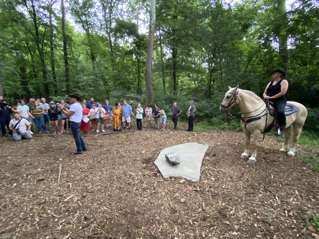 Artist Heidi Wiren Barlett sits on horseback with a man with a cowboy hat speaks to the public in a performance for Bartlett's Upriver artwork on the Karl Stirner Arts Trail in Easton, Pennsylvania