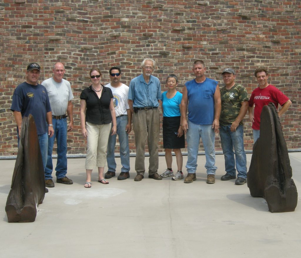 Artist Karl Stirner stands with Michiko Okaya, Jim Toia, and others behind Stirner's Hounds of Hell metal sculpture and in front of the Williams Visual Arts Building's brick exterior on the campus of Lafayette College in Easton, Pennsylvania.