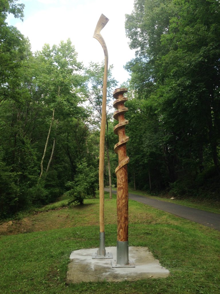 The wooden sculpture Nobori by Loren Madsen, carved from wood to create two rod-like objects, one of which looks like a screw in the top half, on the Karl Stirner Arts Trail in Easton, Pennsylvania