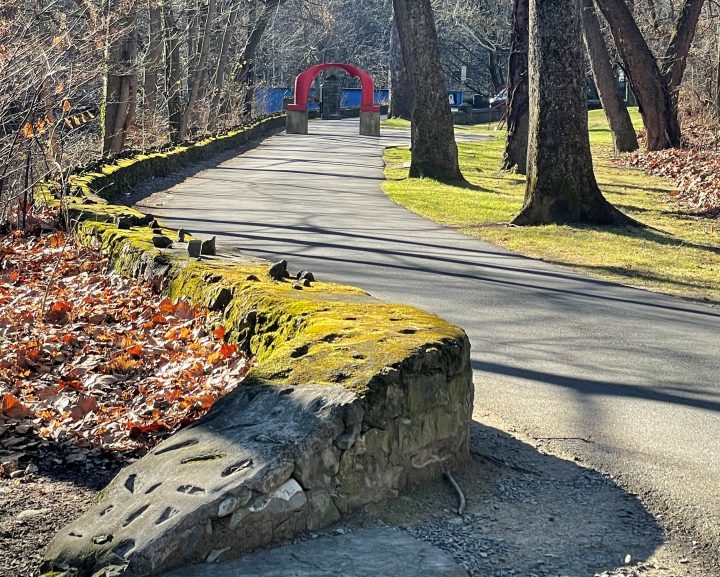 A view of Bushkill Creek, a moss-covered wall, and a stretch of the Karl Stirner Arts Trail in Easton, Pennsylvania, including the iconic red arch sculpture