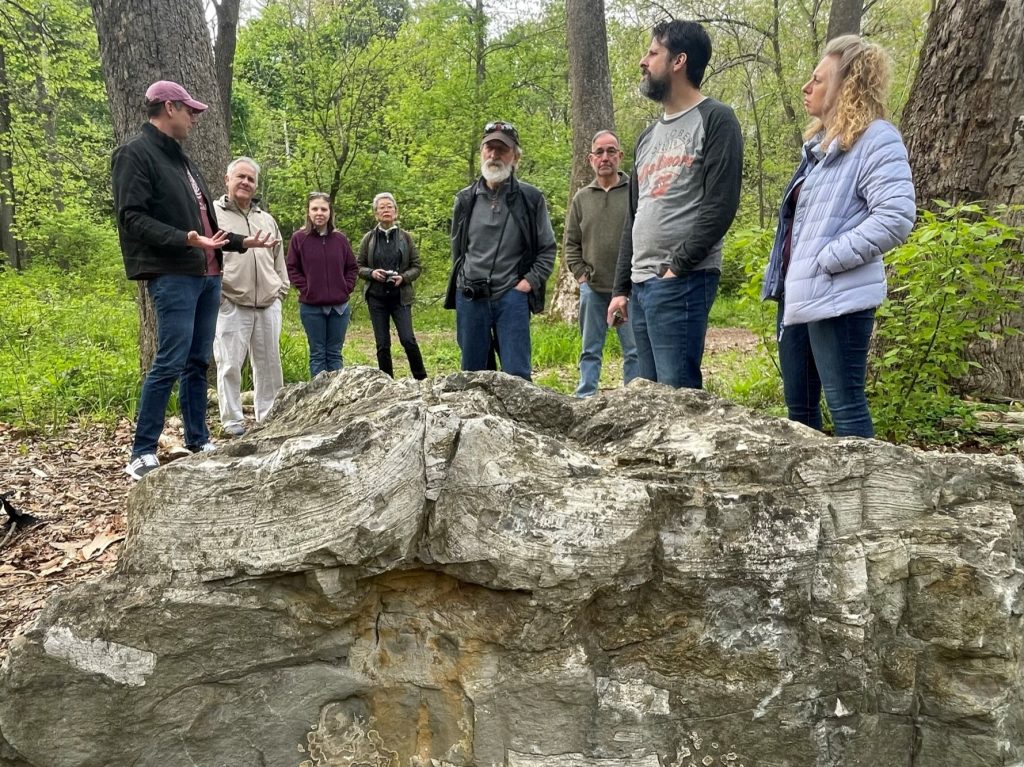 With a large rock in the foreground, Lafayette College geology professor Dave Sunderlin talks to a group during the Walk with Profs event on the Karl Stirner Arts Trail in Easton, Pennsylvania.