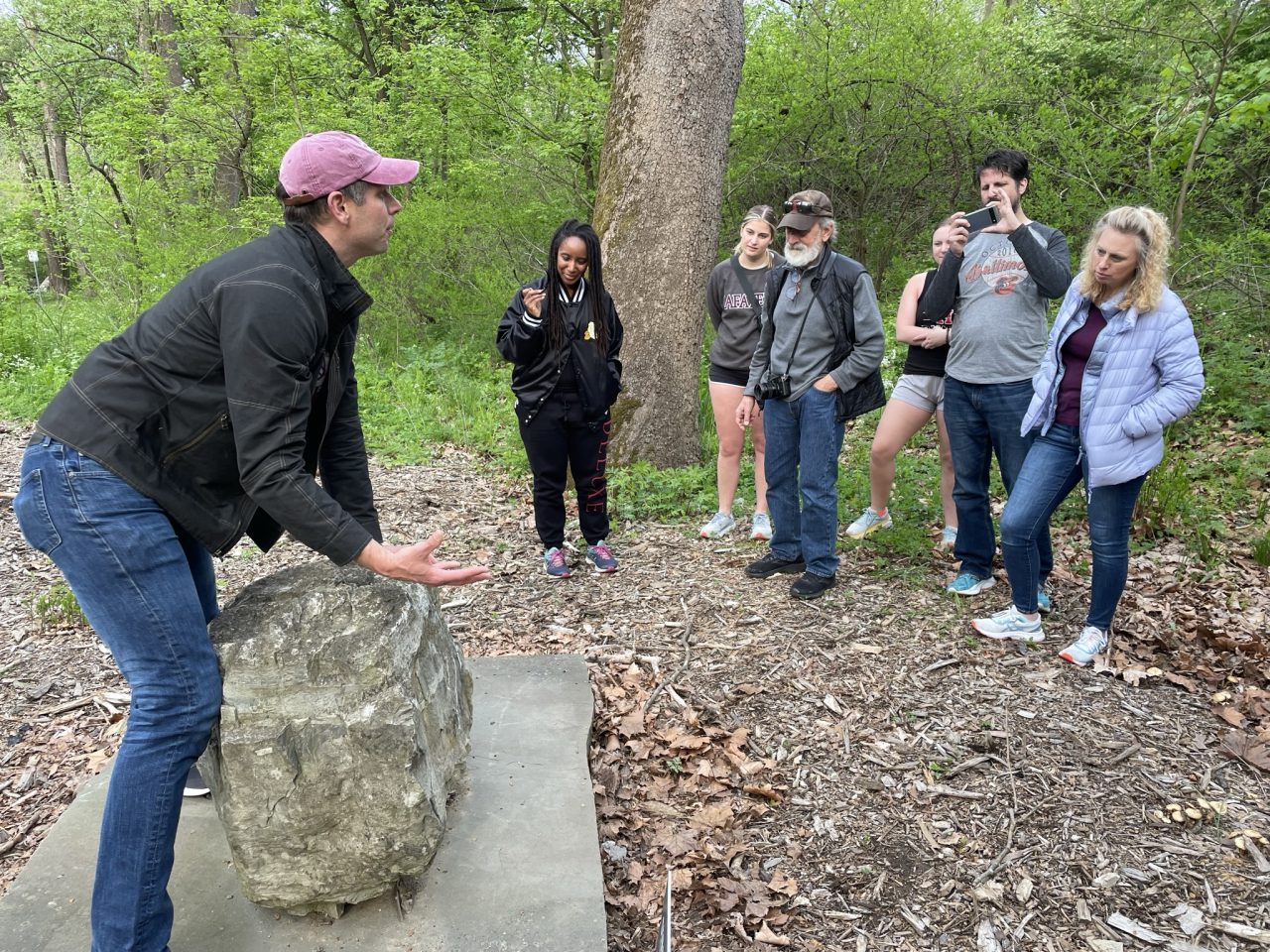 Lafayette College geology professor Dave Sunderlin stands by a large rock and talks to several people during the Walk with Profs event on the Karl Stirner Arts Trail in Easton, Pennsylvania.