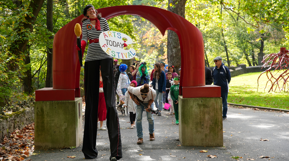 A stilt walker leads a parade of children in costume by the red arch sculpture on the Karl Stirner Arts Trail in Easton, Pennsylvania
