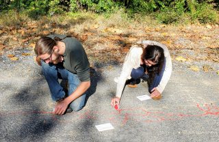 A man and a woman place red sand into cracks on the Karl Stirner Arts Trail in Easton, Pennsylvania, as part of the Red Sand Project.