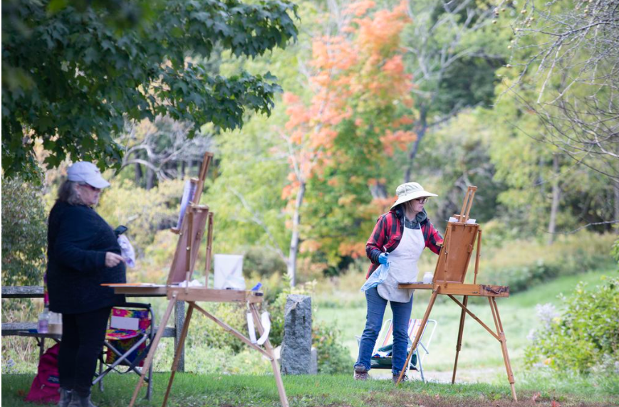 Two women paint on easels outdoors.
