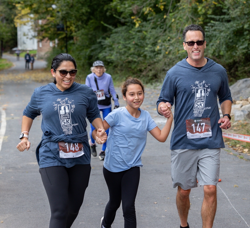 A man, girl, and woman hold hands as they participate in the Artful Dash 5K Walk/Run held on the Karl Stirner Arts Trail in Easton, Pennsylvania.