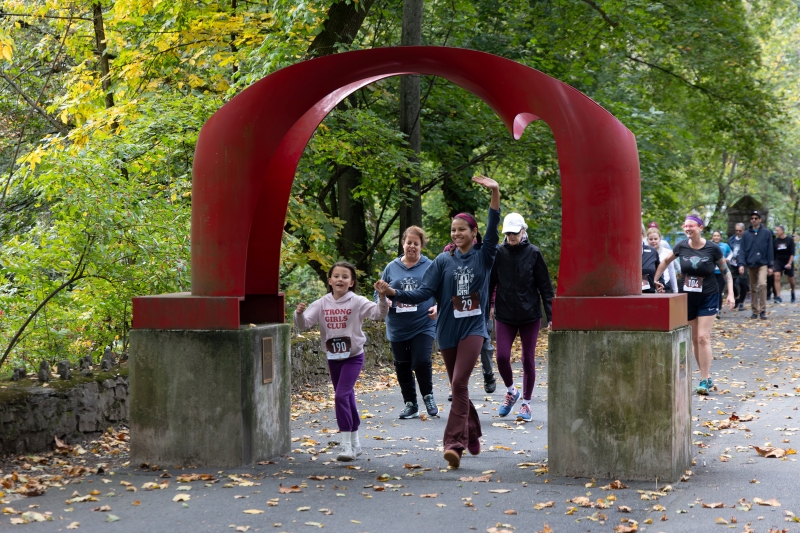 Two children holding hands pass through the red arch sculpture during the Artful Dash 5K Walk/Run held on the Karl Stirner Arts Trail in Easton, Pennsylvania.