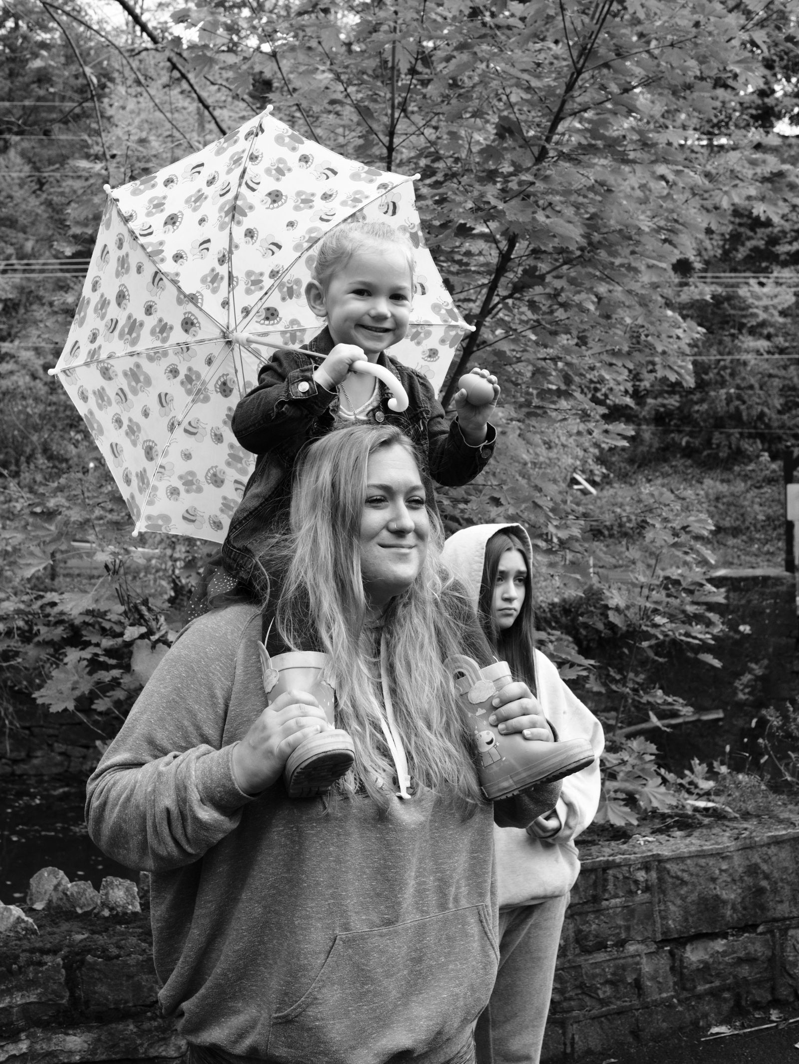 A mother and her two girls, the younger one a toddler on her shoulders holding an umbrella, watch the Come As You Art/Arf children and pets' costume parade on the Karl Stirner Arts Trail in Easton, Pennsylvania.