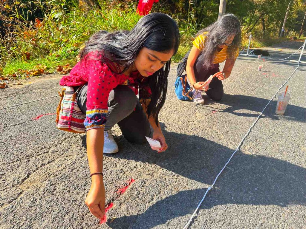 Two people fill cracks in the pavement with red sand during the Walk for the Missing and Stolen event as part of the Red Sand Project on the Karl Stirner Arts Trail in Easton, Pennsylvania.