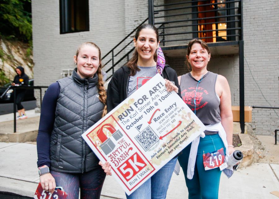 Lynn Schoof and two other women hold a poster promoting the Artful Dash 5K Run/Walk, an annual fundraiser she organizes to benefit the Karl Stirner Arts Trail in Easton, Pennsylvania.