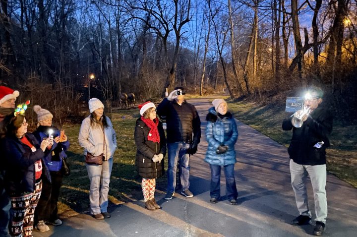 A group of people gather while someone plays the trumpet at night during the Sixth Annual Winter Solstice Walk on the Karl Stirner Arts Trail in Easton, Pennsylvania.
