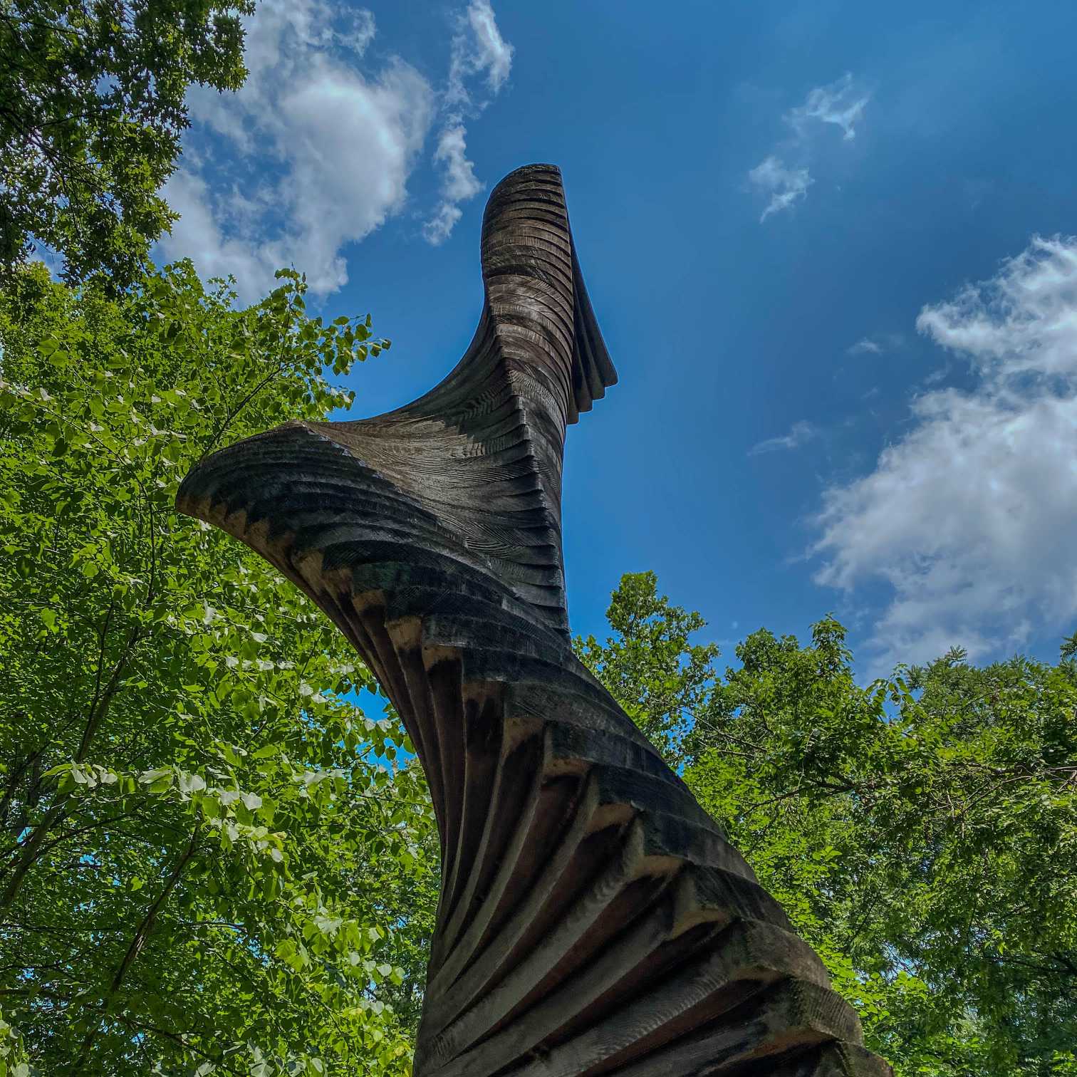 A view from below shows the spirals of the wooden Easton Ellipse sculpture along with blue sky, white clouds and green trees on the Karl Stirner Arts Trail in Easton, Pennsylvania.