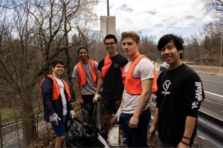 Five Lafayette College students, with four wearing orange vests, pause for a group photo during a cleanup event on the Karl Stirner Arts Trail in Easton, Pennsylvania.