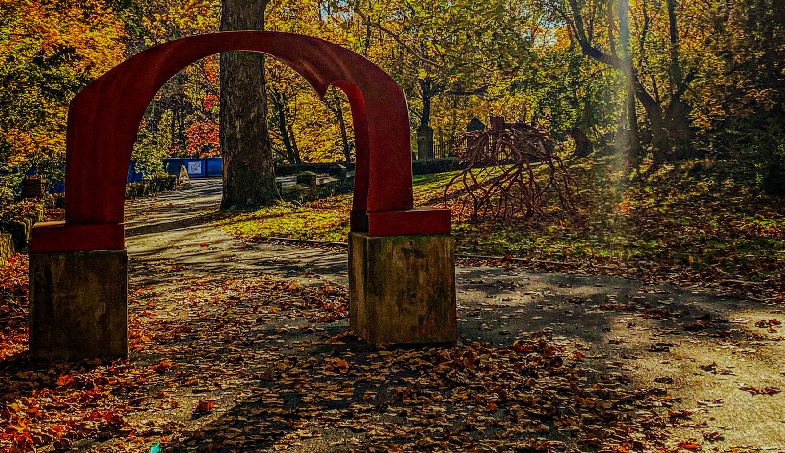The iconic red arch sculpture amid autumn leaves and the Late Bronze Root sculpture behind it on the Karl Stirner Arts Trail in Easton, Pennsylvania.