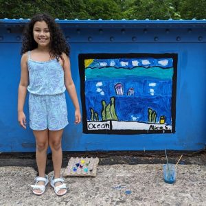 A girl poses next to her painting of an ocean on the Young Masters Wall at the Karl Stirner Arts Trail in Easton, Pennsylvania.