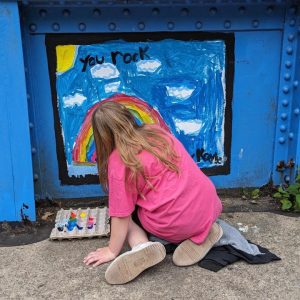 A young girl paints a rainbow with a blue sky and the words "you rock" at the top on the Young Masters Wall at the Karl Stirner Arts Trail in Easton, Pennsylvania.