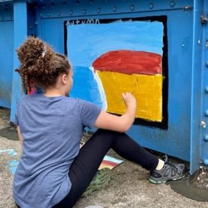 A girl paints a picture with blue, red, and yellow on the Young Masters Wall at the Karl Stirner Arts Trail in Easton, Pennsylvania.